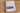 Das Cover des CEWE FOTOBUCH mit dem Titel "Reisetagebuch Korsika" ist zu sehen. Auf der Vorderseite ist ein Bild von Annika und Mathias Koch, die in der Tür ihres Bullis sitzen. Das Cover sieht wie Pergamentpapier aus und ist in der Mitte mit einer einer Holzoptik versehen. Auf der Rückseite sind zwei weitere Bilder von der Natur Korsikas. Das Cover ist mit Cliparts wie einer Weltkarte, Bergen und einem alten VW Bus verziert.