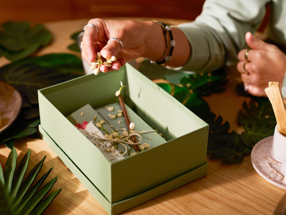 Eine Frau streut getrocknete Blütenknospen in eine Box, in der ein Geschenk liegt.